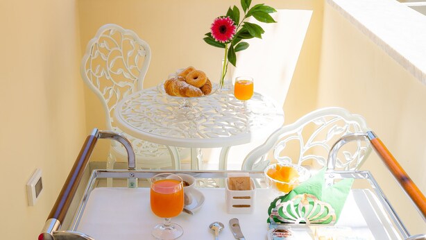A balcony with a glass table, white chairs, and a view of buildings. - L'INCANTO DI CIOFFI ROOMS (Sorrento)