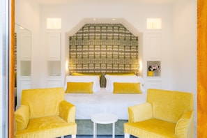A hotel room with a large bed, two yellow armchairs, a small white table, and a patterned headboard.