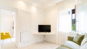 A modern living room with a flat-screen TV mounted on a white wall, a green sofa with yellow trim, and a bright window with sheer curtains. - L'INCANTO DI CIOFFI ROOMS (Sorrento)
