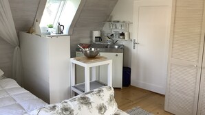 Quarto compacto e bem iluminado com cozinha compacta, uma mesa pequena com uma tigela, uma cama com roupa de cama florida e uma porta.