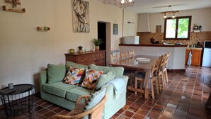 Ein gemütliches Wohnzimmer mit einem grünen Sofa, einem Esstisch mit Stühlen und einer Küche im Hintergrund.