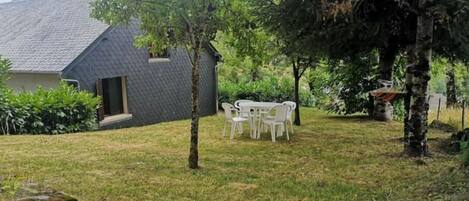 A house with a sloped roof, a small porch, and a grassy yard with a white table and chairs.