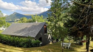 Ein Haus mit geneigtem Dach, umgeben von einem Rasen und Bäumen.