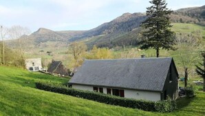 Ein ländliches Haus mit Satteldach, umgeben von üppigen grünen Feldern und Hügeln im Hintergrund.