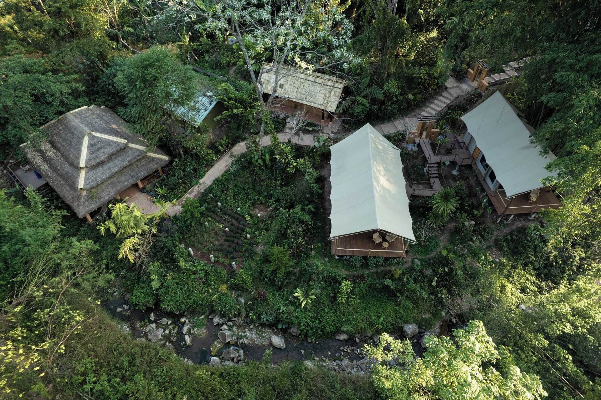 Un refugi ecològic remot amb cabanes de teulada de palla envoltat per un bosc dens.