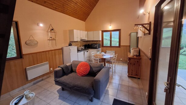 A compact living space with a kitchenette, a sofa with a red cushion, a dining table, and a view of the outdoors through a window.
