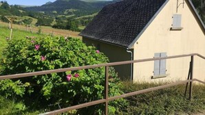 A small, single-story building with a sloped roof, surrounded by lush greenery and hills in the background.