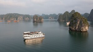 A large boat with multiple decks and a white exterior, floating on calm waters surrounded by lush green islands. - La Regina Classic Cruise (Bai Chay)