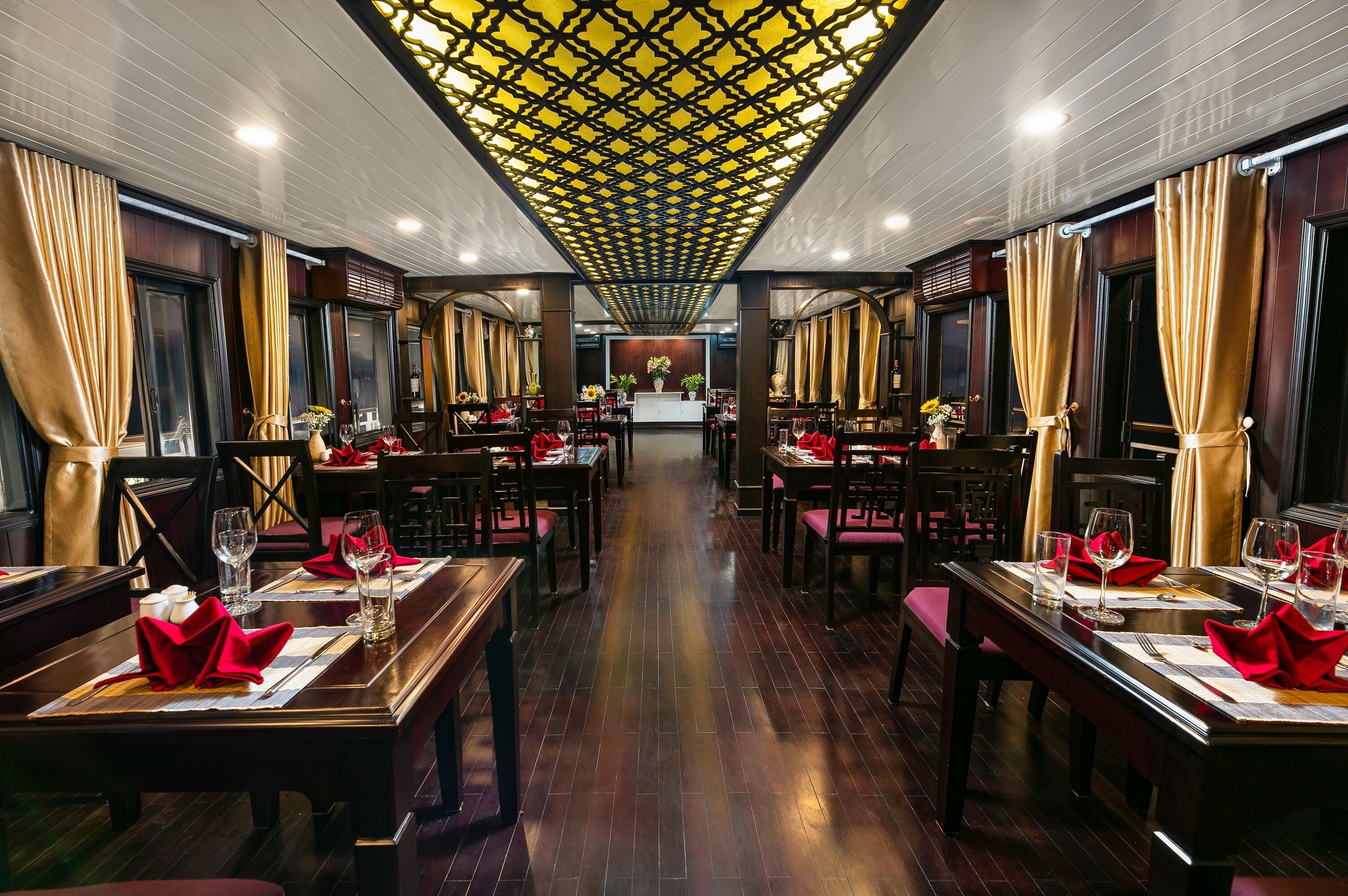 Un restaurant avec des tables et des chaises en bois, un plafond décoré et une allée centrale menant à un comptoir.