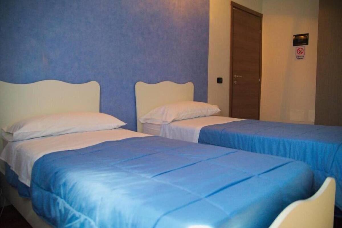 A room with two beds, each with a white headboard and blue bedding.