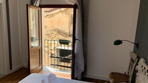 A bedroom with a bed, a nightstand, a lamp, and a view of an outdoor area through an open door. - Cialoma B&B (Palermo)
