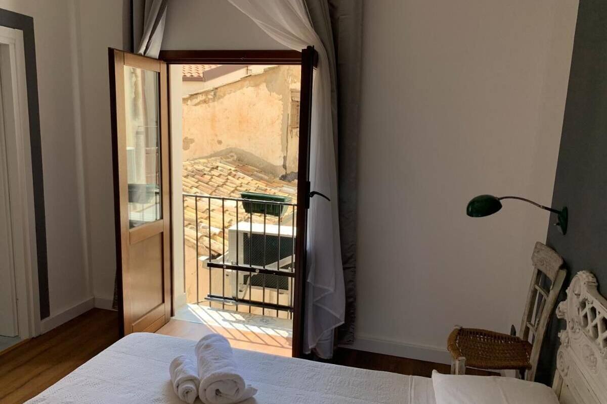 A bedroom with a bed, a nightstand, a lamp, and a view of an outdoor area through an open door.