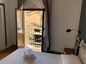 A bedroom with a bed, a nightstand, a lamp, and a view of an outdoor area through an open door. - Cialoma B&B (Palermo)
