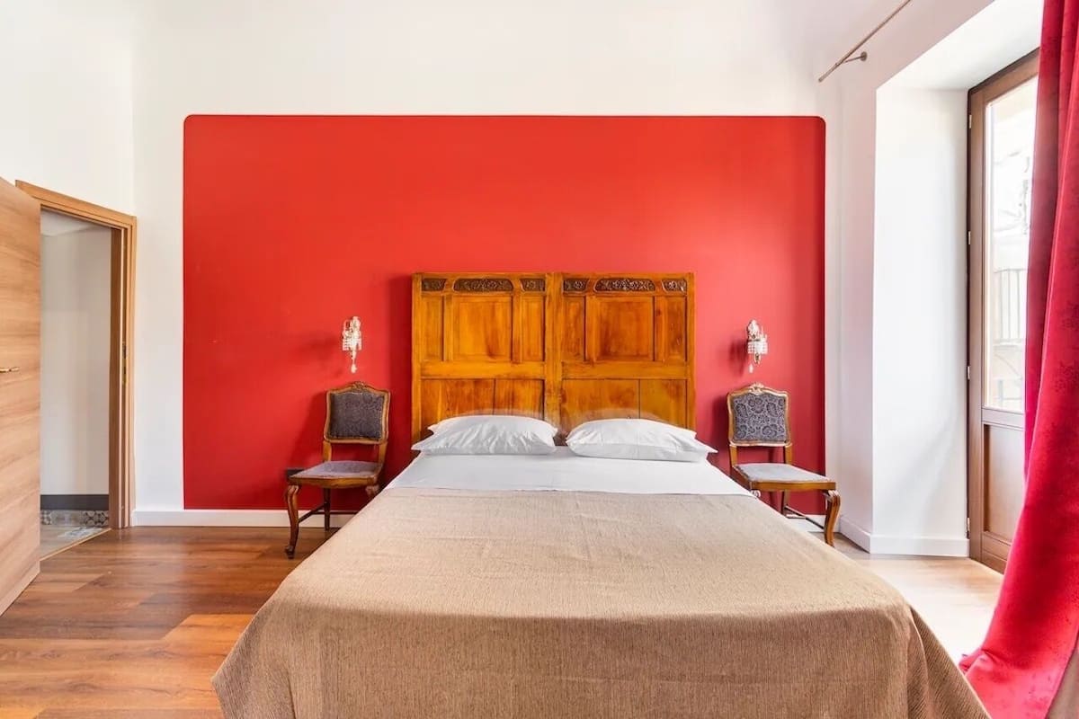A bedroom with a red wall, a wooden headboard, two bedside tables, and a bed with a beige bedspread.