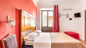 A hotel room with a large bed, a wooden headboard, a red curtain, a television, and a wall-mounted air conditioner. - Cialoma B&B (Palermo)