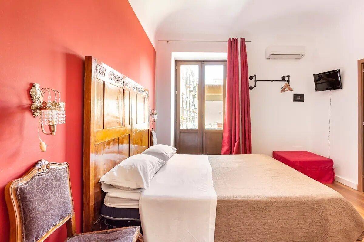 A hotel room with a large bed, a wooden headboard, a red curtain, a television, and a wall-mounted air conditioner.