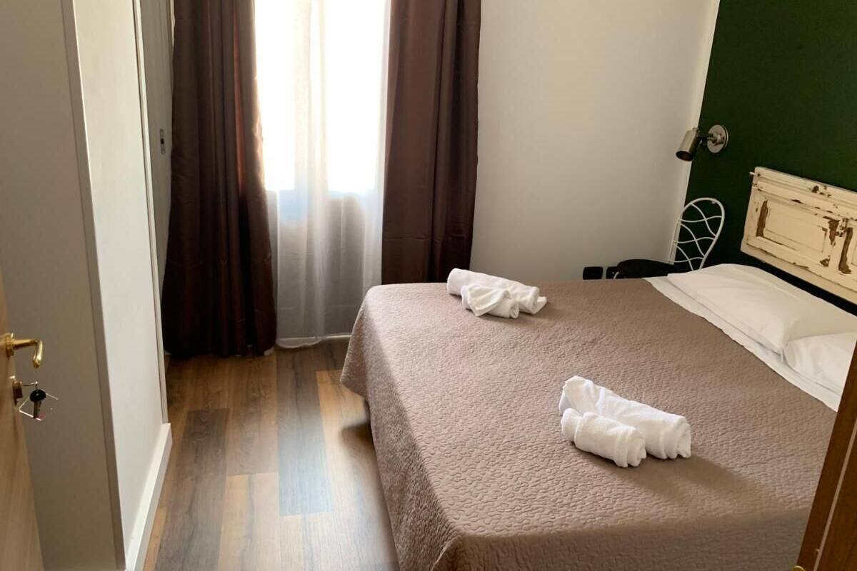 A hotel room with a bed, two towels, a nightstand, and a green wall.