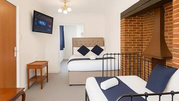 A hotel room with a bed, a small table, a TV, and a brick wall.