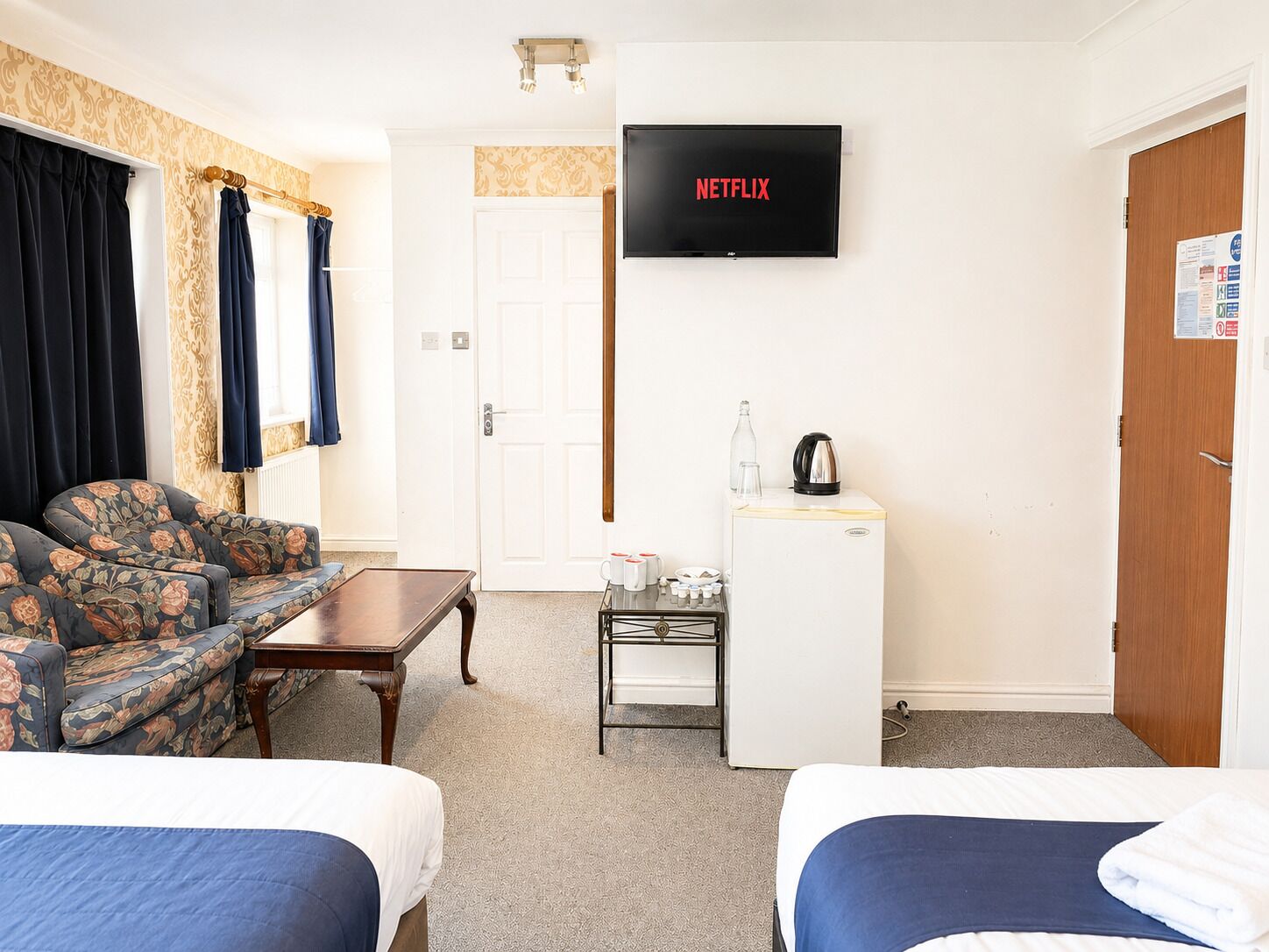 Habitación de hotel con dos camas, un sofá, un televisor, un refrigerador pequeño y una cafetera.