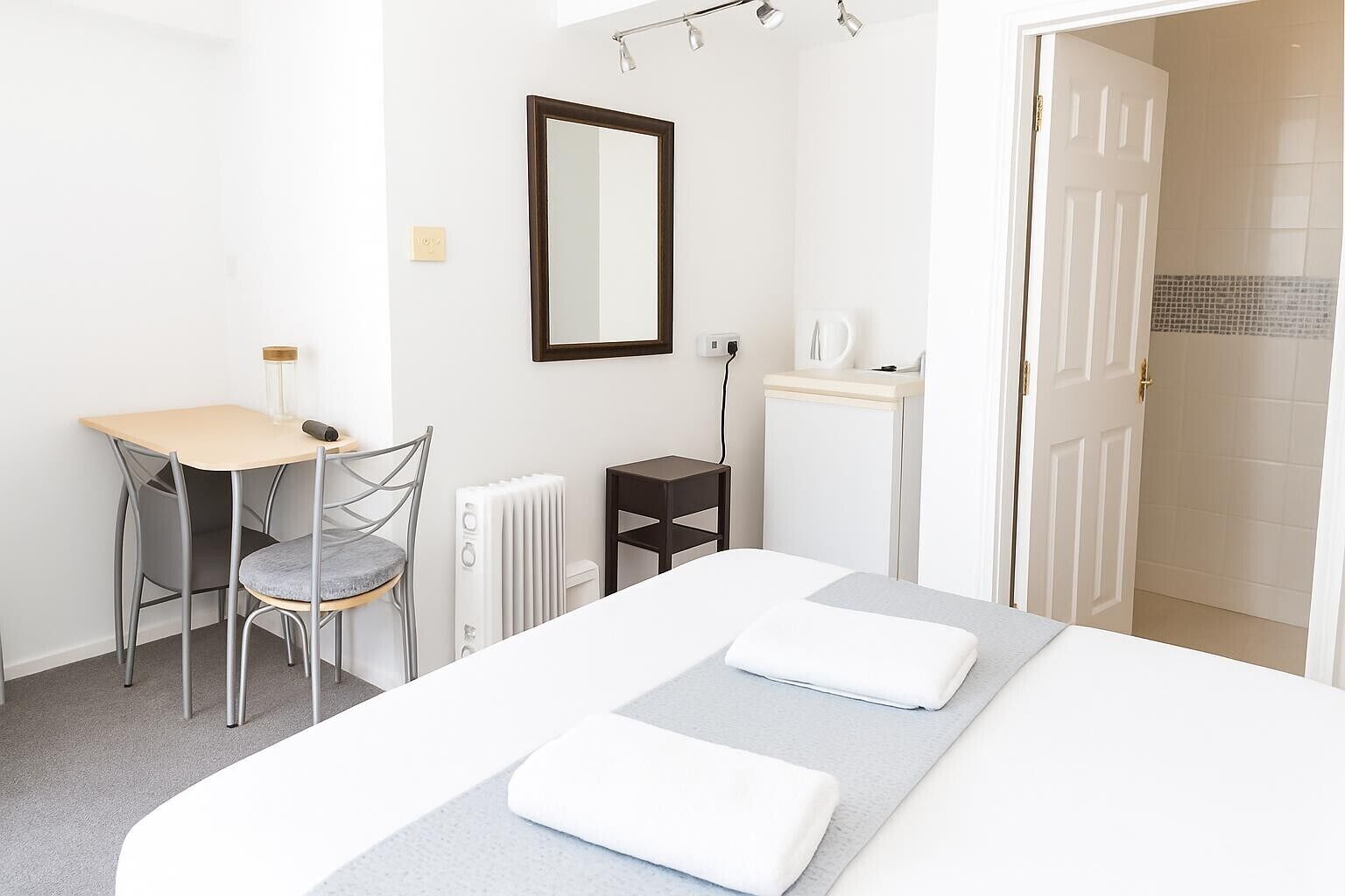 A bedroom with a bed, a desk, a chair, a radiator, a mirror, and a door.