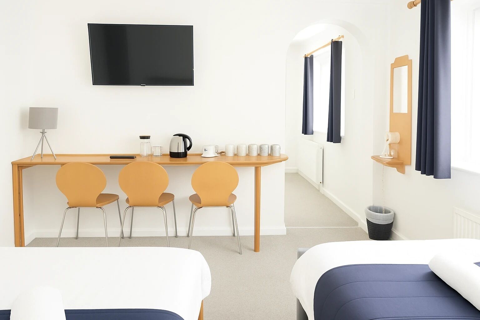 A hotel room with a bed, a desk with chairs, a TV, a coffee maker, and a trash bin.