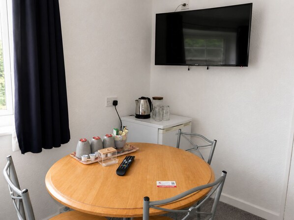 A round wooden table with a remote control, a tray with condiments, and a kettle on a white cabinet. - All Seasons Gatwick Guest House (Horley)