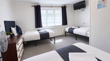 A hotel room with two beds, a dresser, a radiator, a TV, and a window with curtains.