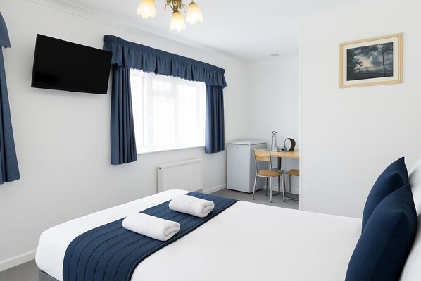 A hotel room with a bed, a desk, a chair, a television, and a picture on the wall. - All Seasons Gatwick Guest House (Horley)