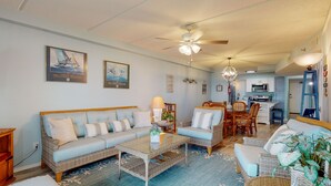 A living room with a sofa, coffee table, and chairs, a dining area with a table and chairs, and a kitchen with cabinets and appliances. - 2nd floor, Boardwalk to the Beach, Shared Pool (Port Aransas)