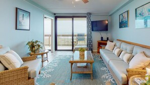 A living room with a large sofa, a coffee table, and a television. There is a balcony with a view of the ocean. - 2nd floor, Boardwalk to the Beach, Shared Pool (Port Aransas)