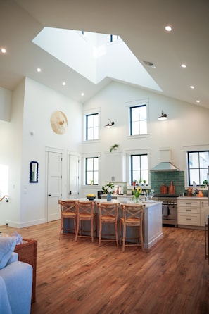 A spacious kitchen with a high ceiling, skylight, and wooden flooring.