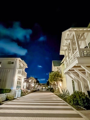 A nighttime view of a coastal street with buildings on either side, a pedestrian walkway, and a clear sky.