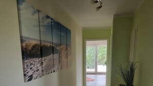 Un couloir doté d’un sol carrelé, d’un ventilateur de plafond, d’une plante en pot et d’une porte donnant sur une pièce lumineuse.