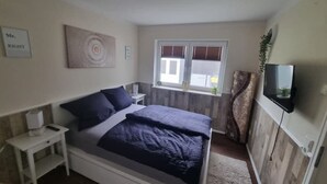 Une chambre à coucher comprenant un lit, une table de chevet, une télévision, une fenêtre et une œuvre d’art.