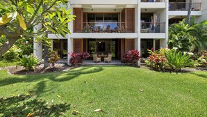 A multi-story building with balconies, a well-maintained lawn, and various plants. - Mauna Lani Condo | Short Walk to Beach (Kamuela)