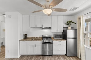 A modern kitchen with white cabinets, a stainless steel stove, a microwave, and a refrigerator.