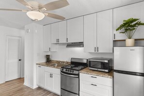 A modern kitchen with white cabinets, a stainless steel stove, a microwave, and a refrigerator.