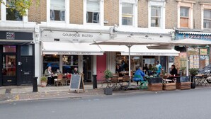Et gadesyn af en moderne bistro åben hele dagen med udeservering og en synlig tavlemenu.