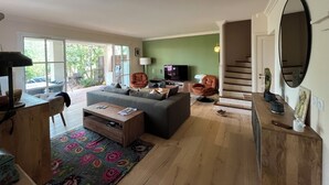 Ein Wohnzimmer mit Sofa, Sesseln, einem Couchtisch und einem Fernseher. Eine Treppe führt zu einer weiteren Ebene.