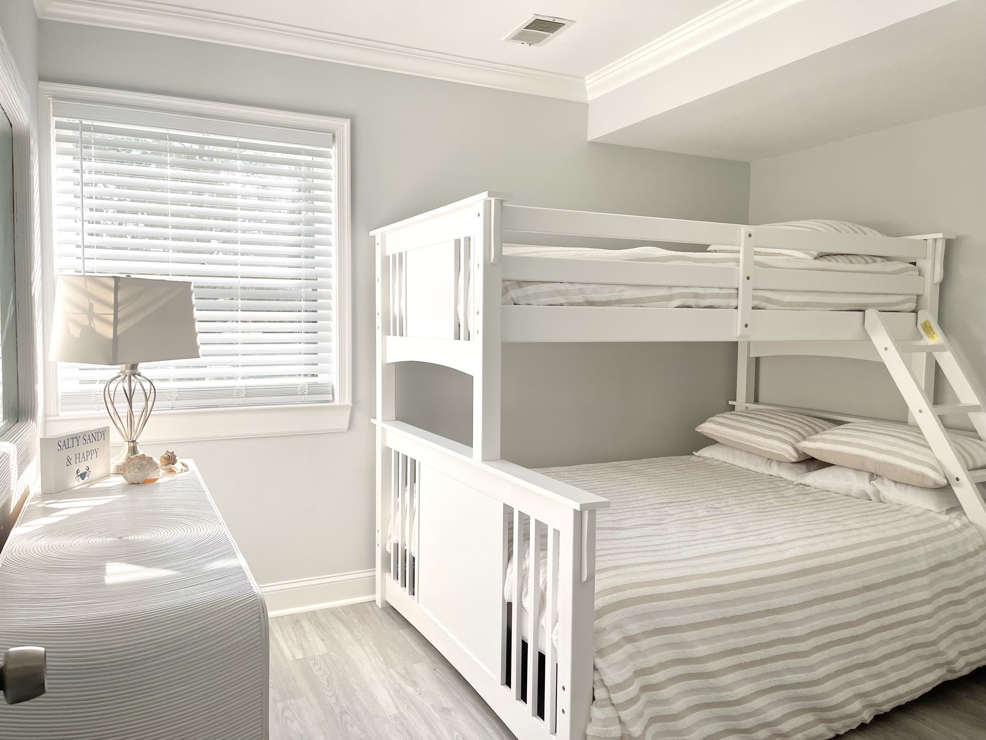 A child's bedroom with bunk beds, a desk with a lamp, and a window with blinds.