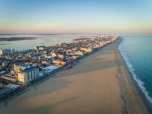 Eine Luftaufnahme einer Küstenstadt mit einem langen Strand, Gebäuden und einem Pier.