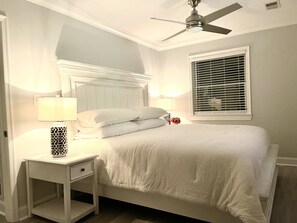 Ein Schlafzimmer mit Bett, Nachttischen, Deckenventilator und einem Fenster mit Jalousien.