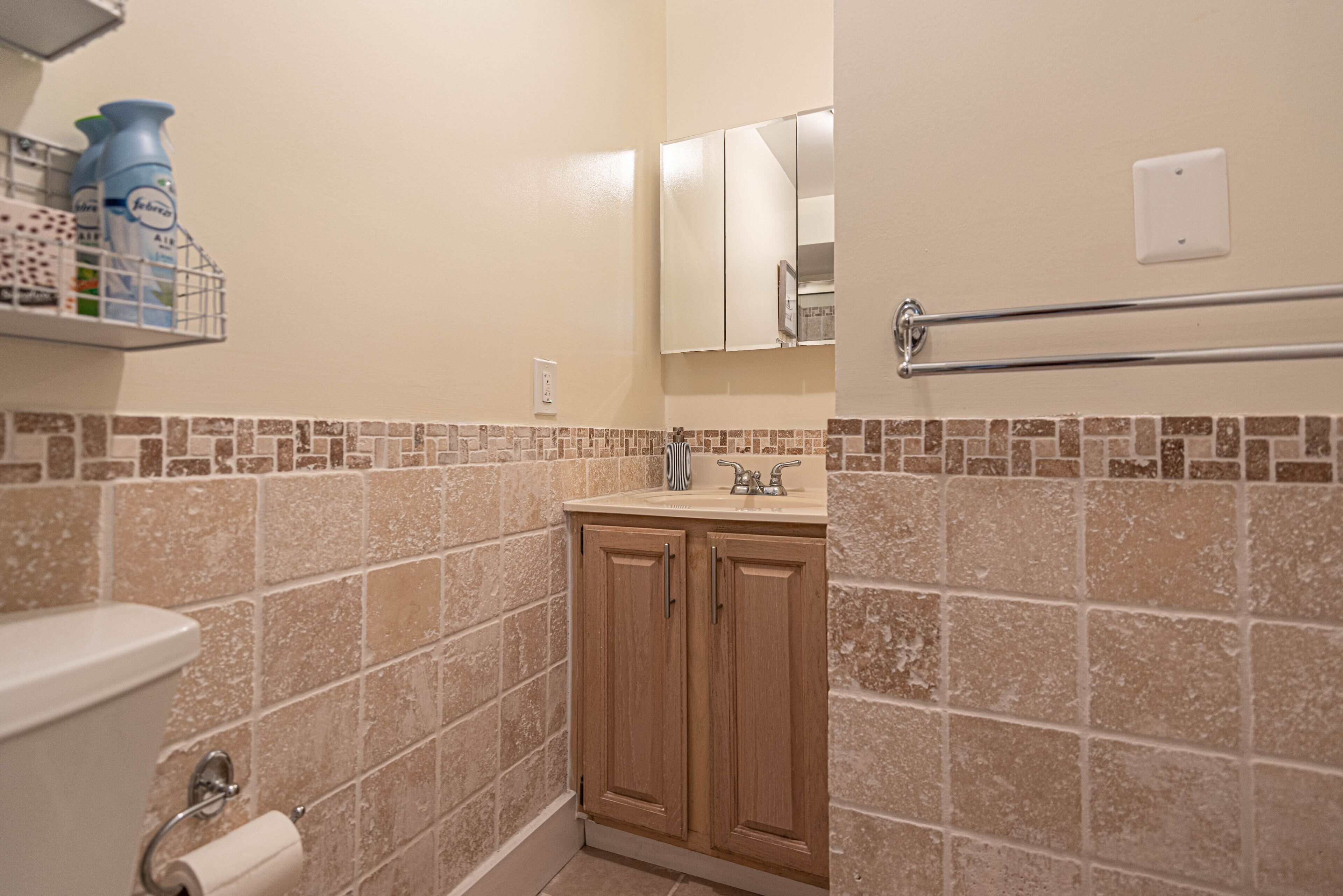 A bathroom with a toilet, a sink, and a mirror. There are toiletries on a shelf.