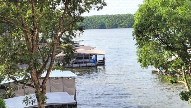 A lakeside view with a dock and covered structures, surrounded by trees. - Dream Condo with Perfect Location for All The Fun! (Osage Beach)