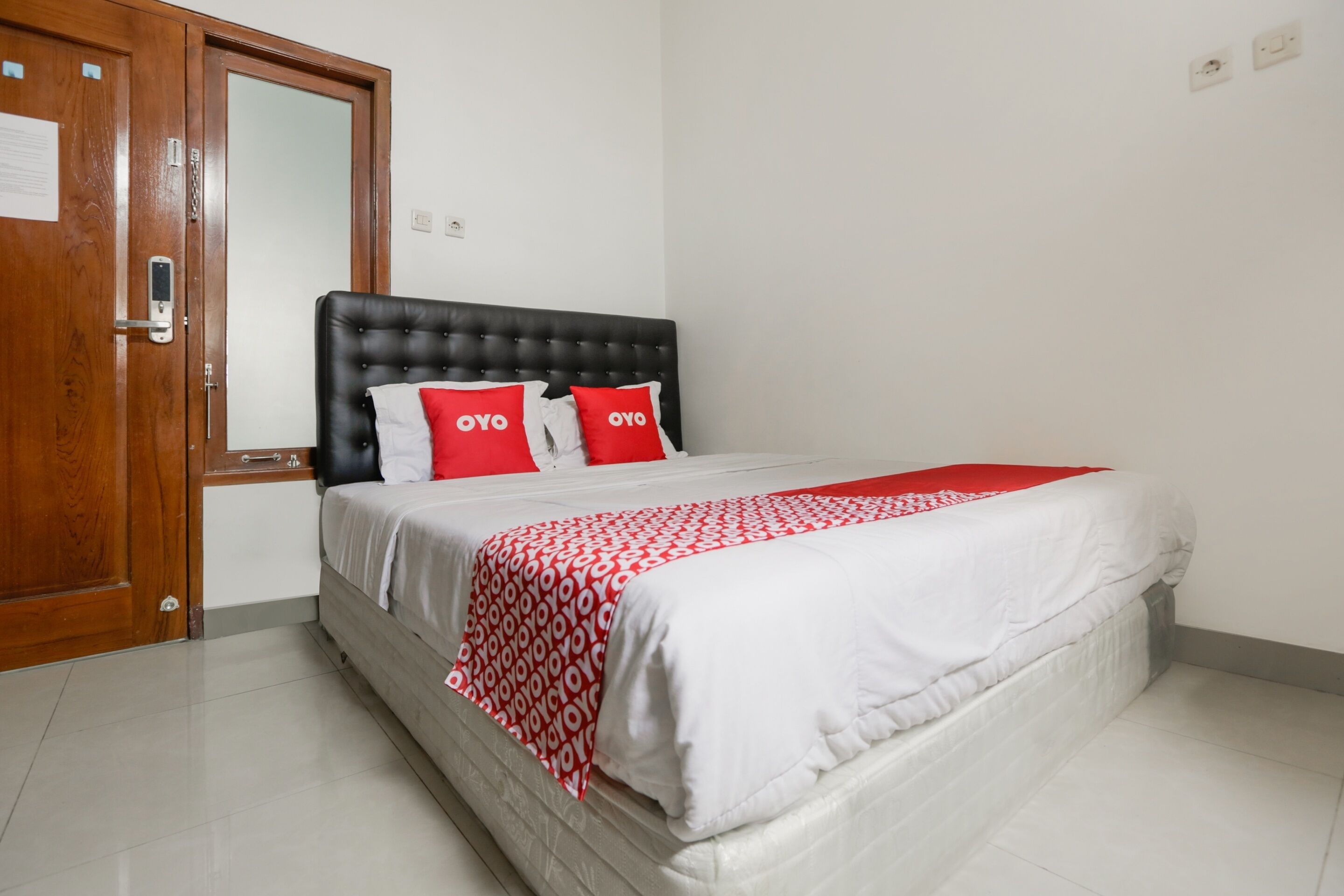 Una cama cuidadosamente arreglada con una colcha de cuadros rojos y blancos y dos almohadas rojas con el texto "OYO".