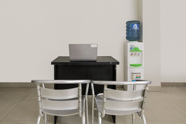 Un petit bureau avec un ordinateur portable posé sur le bureau, un distributeur d’eau et deux chaises.