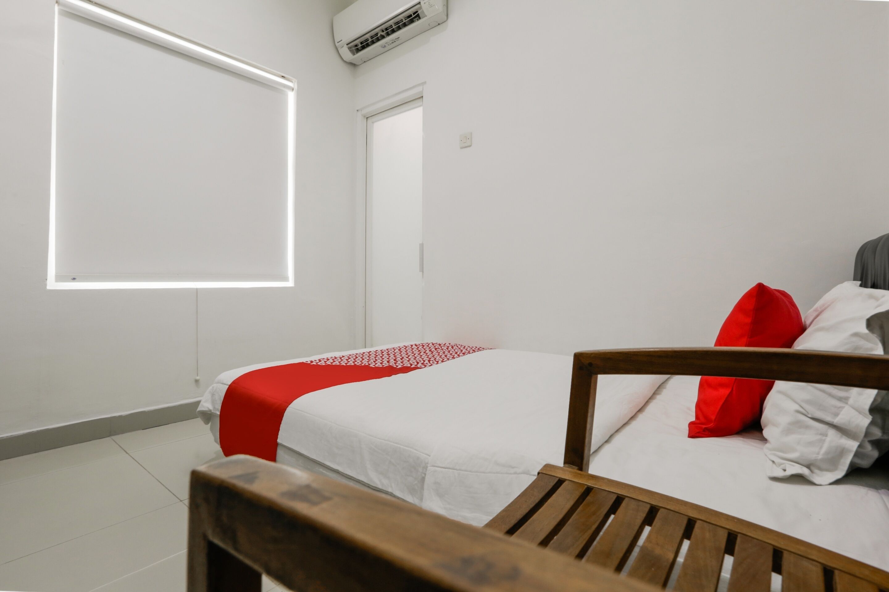 A bedroom with a bed, a wooden bench, a window with blinds, and a door.
