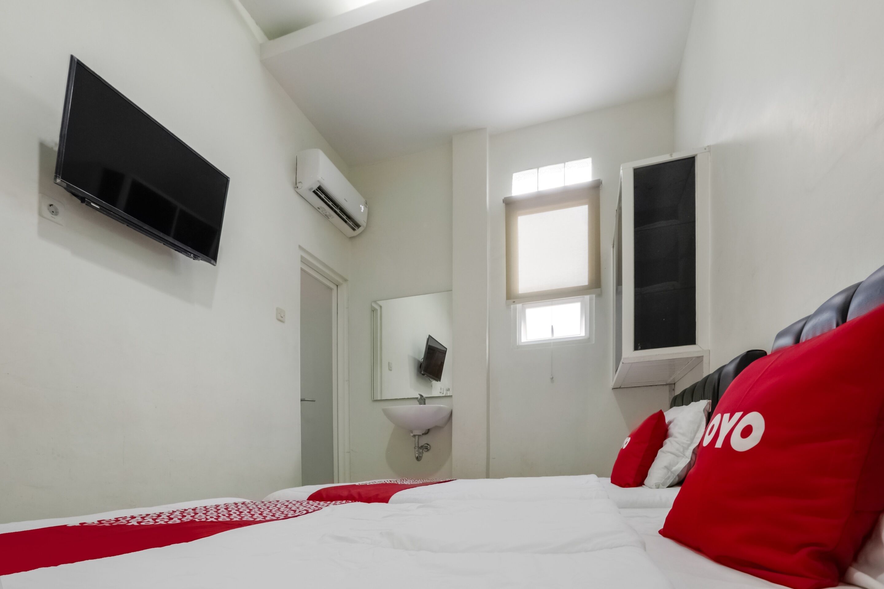 Ein Hotelzimmer mit Bett, Wandfernseher, Fenster und Waschbecken.