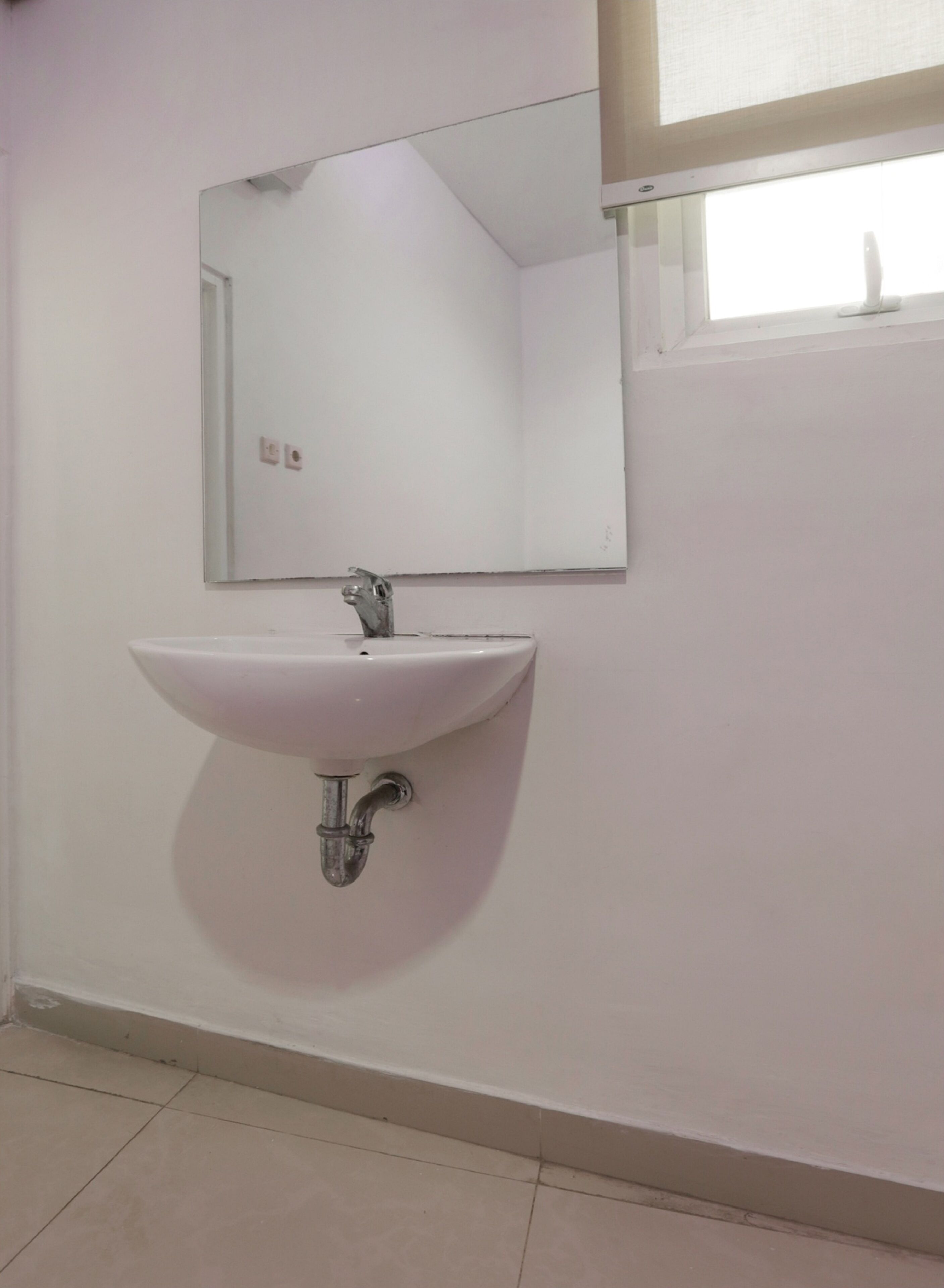 A bathroom with a white sink, a mirror, and a window above the sink.