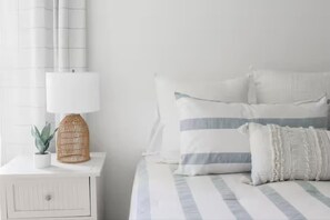 A bedroom with a bed, pillows, a bedside table, a lamp, and a small plant.